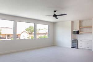 Unfurnished room with beverage cooler, light colored carpet, baseboards, a ceiling fan, and a bar
