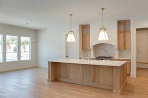 Kitchen with light wood-style floors, light countertops, a sink, and a kitchen island with sink