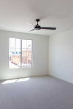 Carpeted empty room with a ceiling fan and baseboards