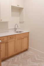 Kitchen with a sink, light countertops, light brown cabinets, and baseboards