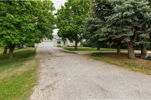 View of property hidden behind natural elements featuring concrete driveway, a front lawn, stone siding, and an attached garage