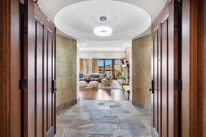 Hallway with light stone finish flooring, a chandelier, and a tray ceiling