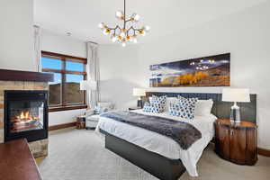 Carpeted bedroom featuring baseboards, a fireplace, and a chandelier