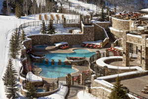 Snow covered pool with a jacuzzi, a community pool, fence, and a patio