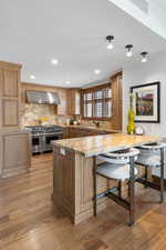 Kitchen with wall chimney range hood, appliances with stainless steel finishes, decorative backsplash, a kitchen bar, and light wood-style floors