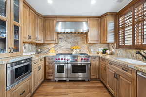 Kitchen featuring appliances with stainless steel finishes, wall chimney exhaust hood, a sink, light stone countertops, and backsplash