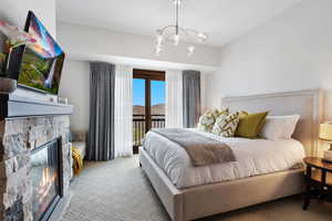 Carpeted bedroom with access to exterior, a chandelier, and a fireplace