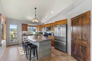 Kitchen featuring stainless steel appliances, brown cabinetry, backsplash, vaulted ceiling, and a kitchen bar