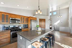 Kitchen featuring appliances with stainless steel finishes, brown cabinetry, a center island, backsplash, and a kitchen breakfast bar