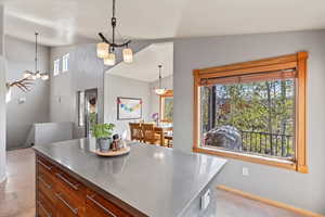 Kitchen featuring stainless steel counters, a chandelier, decorative light fixtures, baseboards, and a center island