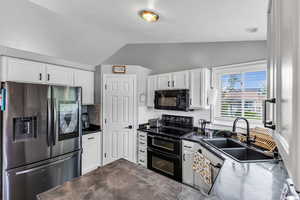 Kitchen featuring black appliances, lofted ceiling, a sink, and white cabinetry