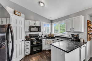 Kitchen featuring black appliances, a peninsula, a sink, lofted ceiling, and decorative backsplash