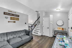 Living room featuring dark wood finished floors, stairway, and lofted ceiling
