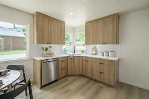 Kitchen with stainless steel dishwasher, a sink, tasteful backsplash, light wood-style flooring, and light countertops