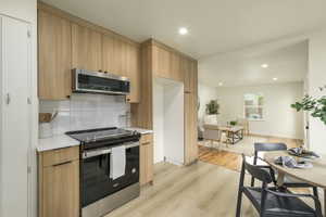 Kitchen featuring stainless steel appliances, light countertops, decorative backsplash, light wood-style flooring, and recessed lighting