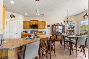 Kitchen featuring stainless steel appliances, a chandelier, a kitchen breakfast bar, light stone countertops, and a textured ceiling