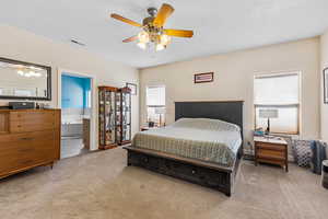Bedroom with light colored carpet, ensuite bath, a textured ceiling, and a ceiling fan