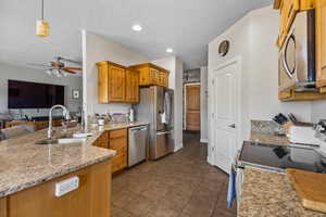 Kitchen featuring stainless steel appliances, a sink, a ceiling fan, light stone counters, and dark tile patterned flooring