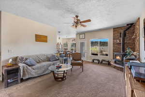 Living room featuring a wood stove, a ceiling fan, and a textured ceiling