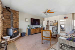 Living area featuring a wood stove, ceiling fan, and a textured ceiling