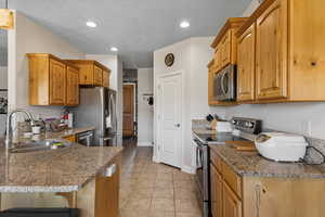 Kitchen with stainless steel appliances, a sink, stone countertops, a peninsula, and a breakfast bar