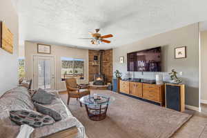 Living area featuring a wood stove, ceiling fan, baseboards, and a textured ceiling