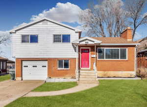 Split level home with a garage, a chimney, a front lawn, brick siding, and concrete driveway