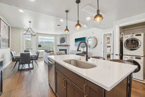 Kitchen with stacked washing machine and dryer, a sink, stainless steel dishwasher, light countertops, and hanging light fixtures
