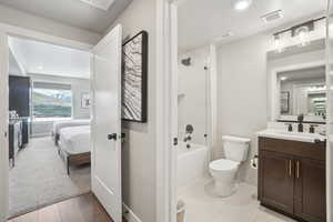 Ensuite bathroom featuring toilet, vanity, baseboards, and shower / bathtub combination