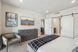 Bedroom with a barn door, light colored carpet, recessed lighting, ensuite bath, and baseboards
