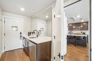 Kitchen with stainless steel microwave, a sink, light wood finished floors, dark brown cabinets, and light countertops