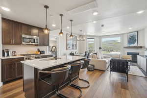 Kitchen featuring stainless steel microwave, a sink, open floor plan, dark brown cabinets, and wood-type flooring