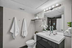 Full bathroom with toilet, vanity, a shower with shower curtain, and a textured wall