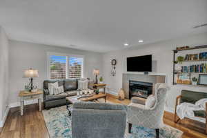 Living room featuring baseboards, a tiled fireplace, wood finished floors, and recessed lighting