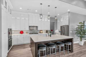Kitchen with appliances with stainless steel finishes, a sink, light wood-type flooring, a center island with sink, and recessed lighting