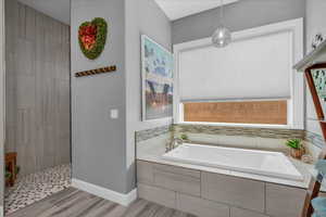 Bathroom featuring a garden tub, wood finished floors, a walk in shower, and baseboards