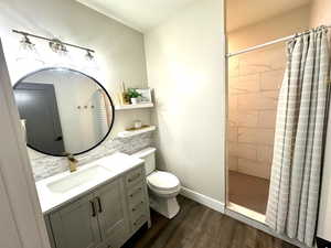 Bathroom with wood finished floors, a tile shower, toilet, vanity, and baseboards