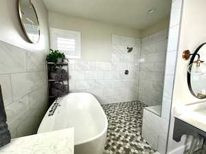 Full bath featuring tile walls, a soaking tub, tiled shower, and vanity