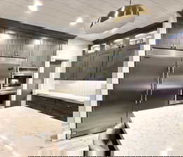 Kitchen with stainless steel appliances, light wood-type flooring, tasteful backsplash, light stone countertops, and decorative light fixtures