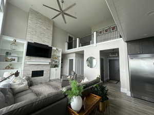 Living area featuring a towering ceiling, ceiling fan, a fireplace, wood finished floors, and baseboards