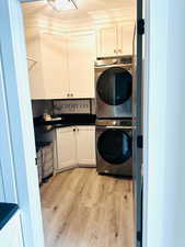 Laundry area featuring estacked washer and dryer, cabinet space, light wood-type flooring, and a textured ceiling