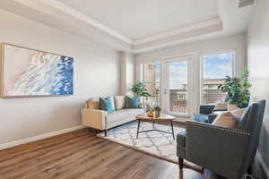 Living room featuring ornamental molding, a tray ceiling, wood finished floors, and baseboards