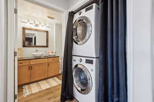 Clothes washing area featuring stacked washer / drying machine, light wood finished floors, and a sink