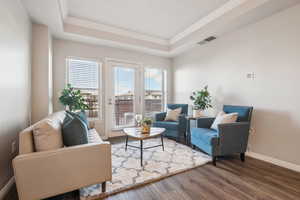 Living area with a tray ceiling, baseboards, dark wood-type flooring, and ornamental molding