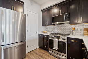 Kitchen with stainless steel appliances, decorative backsplash, light wood-style floors, and dark brown cabinetry