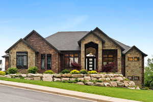 View of front of property with stone siding, a front yard, a shingled roof, and brick siding