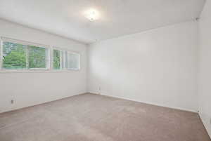 Spare room featuring light carpet, a textured ceiling, and baseboards