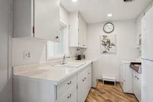 Kitchen featuring a sink, separate washer and dryer, white cabinets, light wood-type flooring, and freestanding refrigerator