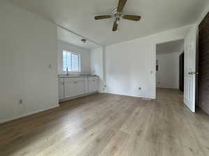 Unfurnished living room with a sink, ceiling fan, light wood finished floors, and baseboards