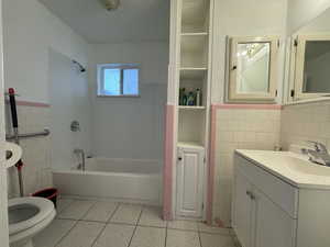 Full bathroom with tile walls, tile patterned flooring, shower / bath combination, a wainscoted wall, and vanity